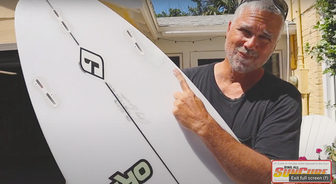 Ding All Dale holding a repaired Fire Wire surfboard. Dale is positioned outside under the sunshine and is smiling.