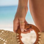 Ripple wave rings in silver and gold worn near a beach setting.