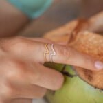 Silver and gold Crest of the Wave ring with adjustable fit, worn on a hand holding a coconut. Handmade jewelry with eco-friendly design.