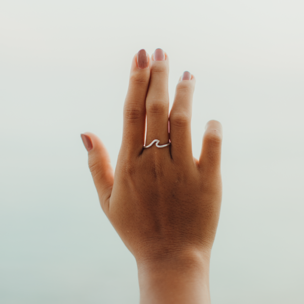 Hand wearing the Pineapple Island Surfer Girl Wave Ring in silver, showcasing its minimalist wave design. Lightweight, adjustable handmade jewelry for stylish looks.