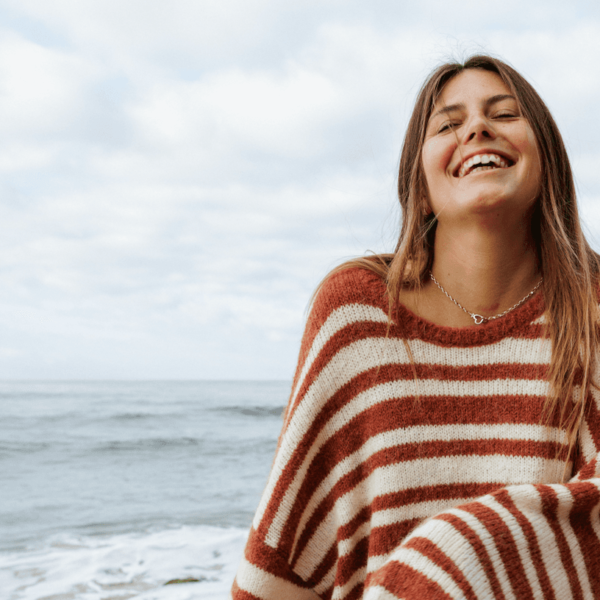 Sisstr Ocean Shores Sweater in rust with white stripes, worn by the beach.