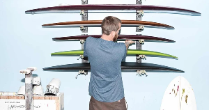 Man organizing colorful surfboards on a wall rack in a workshop. Vissla Surf